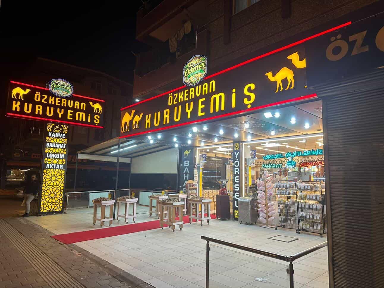 The façade of the Öz Kervan Kuruyemiş shop, lit up in the evening